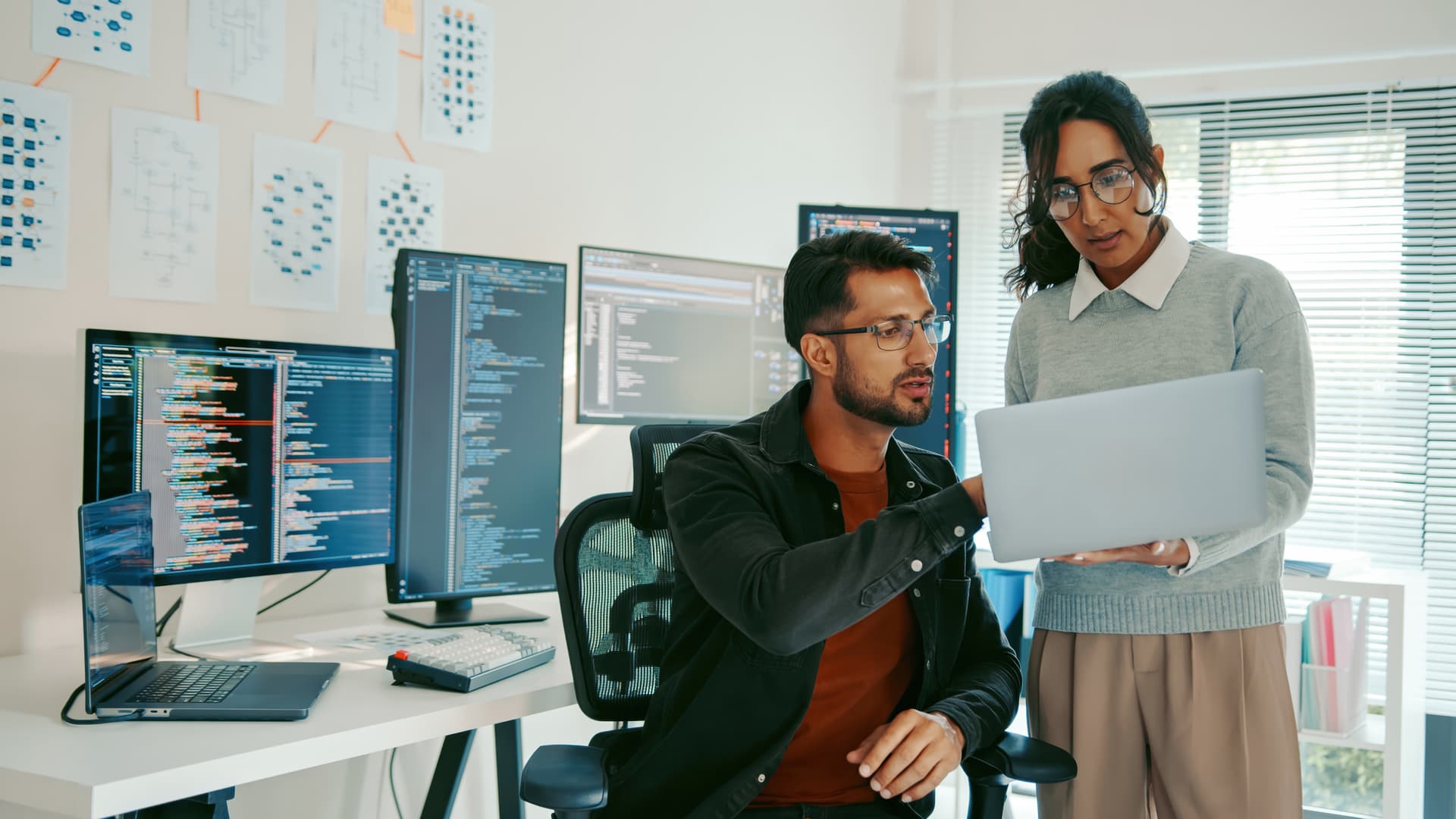 Two individuals collaborating on a laptop, focused on a computer screen in a shared workspace.